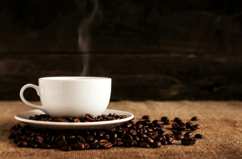 White ceramic mug and saucer with coffee beans on brown textile, illustrating choosing manageable everyday coffee habits